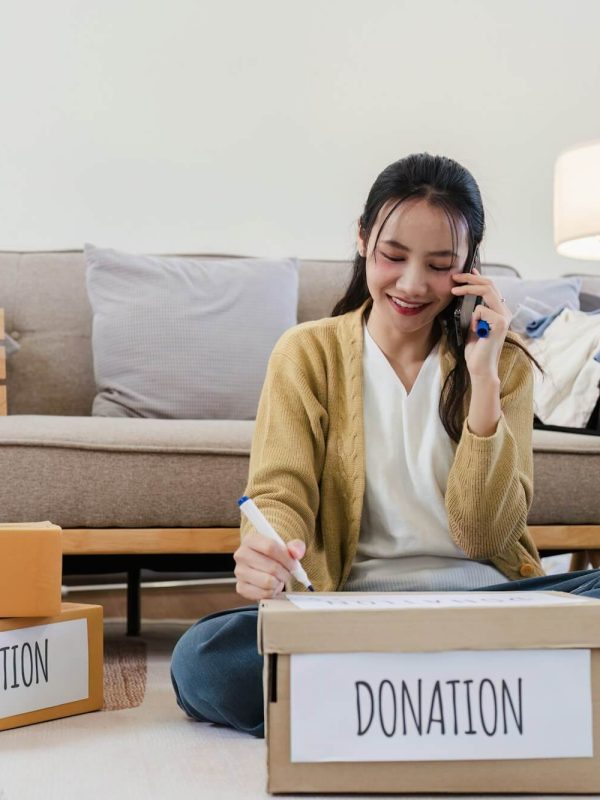 young-woman-asian-of-charity-putting-clothes-in-boxes-with-donations-lettering-and-using-smartphone.jpg